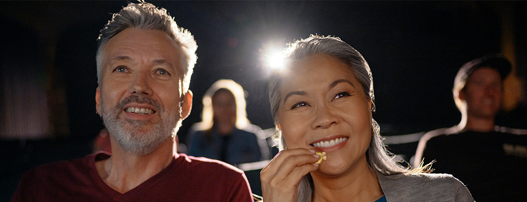 Image of female hearing aid wearer eating popcorn with a male companion in a movie theater